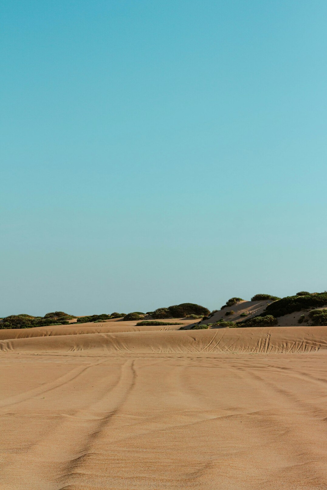 Empty desert road crossing sand dunes under a clear sky